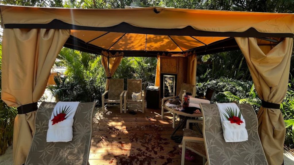 Looking into cabana at Discovery Cove, Orlando. Two lounge chairs with towels on top frame and inside additional chairs and mini fridge.