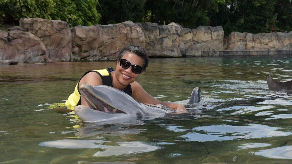 African American woman with sunglasses on with dolphin at Discovery Cove Orlando